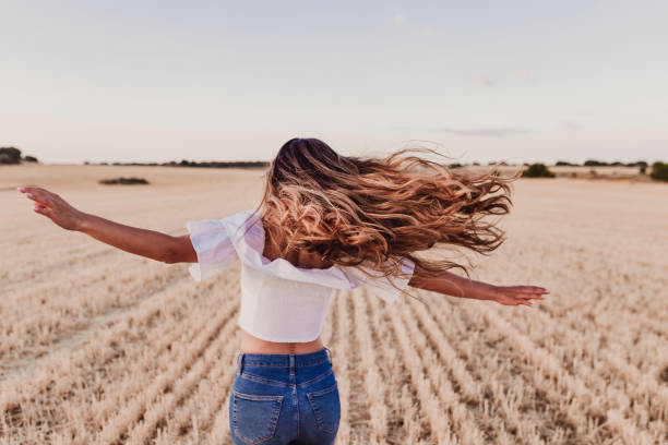 summer girl disfrutando de la naturaleza en el campo amarillo. hermosa joven bailando al aire libre. pelo largo en el viento. felicidad y estilo de vida. vista posterior - cabello largo fotografías e imágenes de stock