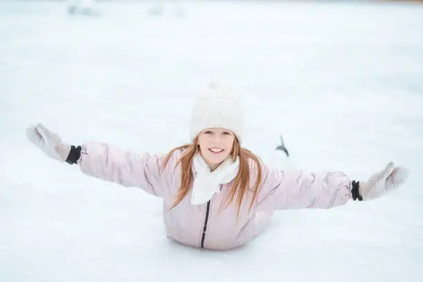 Adorable little girl skating on the ice-rink and having fun outdoors