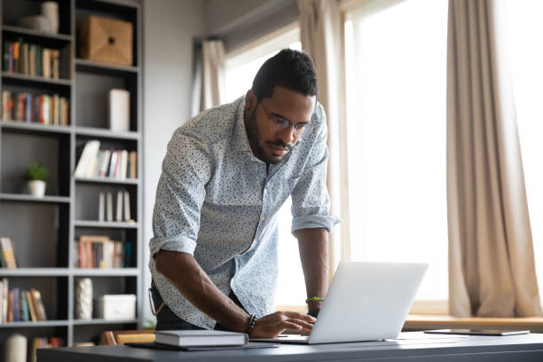 istock Focused african businessman standing at home office desk using laptop 1203044152