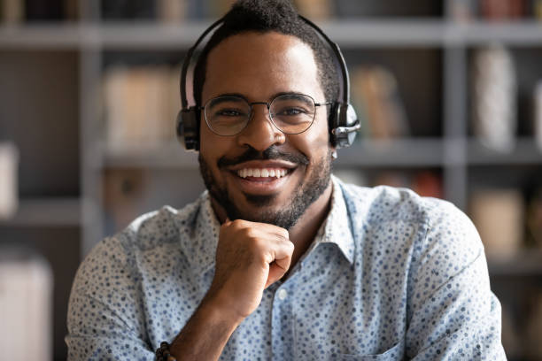 istock Smiling african man professional telemarketer wear headset look at camera 1203044161