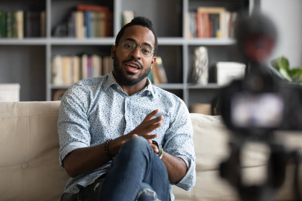 African american hipster man blogger recording vlog on digital camera Millennial african hipster man blogger recording vlog on digital camera sit on sofa in living room, confident young guy vlogger influencer shooting social media video blog on camcorder talk at home influencer photos stock pictures, royalty-free photos & images