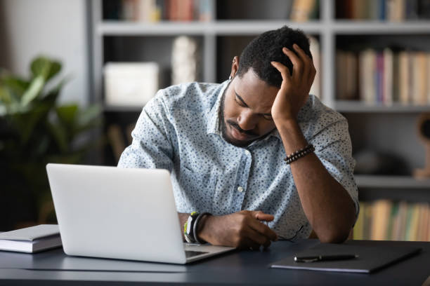 istock Tired bored african employee falling asleep sitting at work desk 1203044195