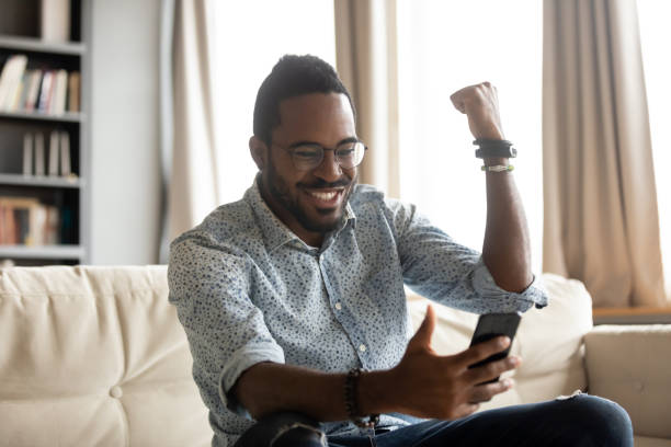 istock Happy african man winner looking at phone celebrating bet win 1203044196