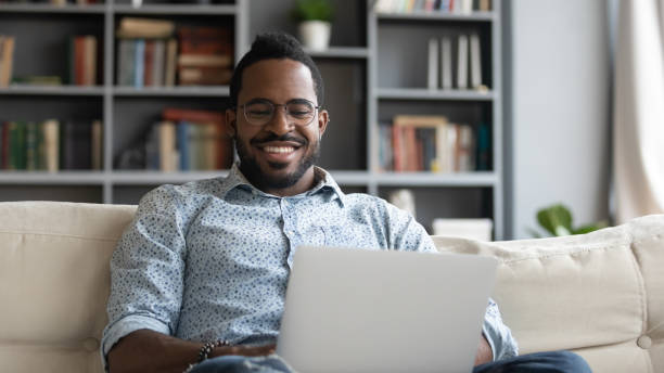 istock Smiling african man using laptop watching movies sit on sofa 1203044213