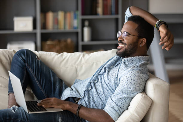 istock Relaxed african man resting on couch using laptop at home 1203044216