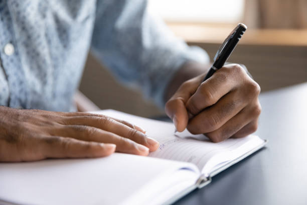 Close up view of african left-handed businessman writing in notebook Close up view of african left-handed businessman writing in notebook, american male hands holding pen making notes planning new appointments information in organizer personal paper planner at desk script stock pictures, royalty-free photos & images