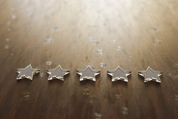 istock 3D render: Five star rating - five transparent acrylic glas stars lying on a wooden table. Selective focus and copy space. 1203049049