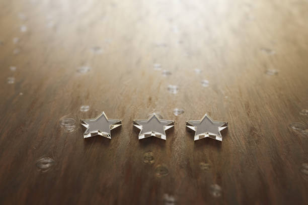 istock 3D render: Three star rating - three transparent acrylic glas star lying on a wooden table. Selective focus and copy space. 1203049087