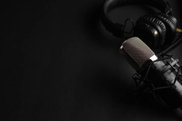 istock Studio black studio microphone with studio headphones on a black background. Banner. Radio, work with sound, podcasts. 1203054697