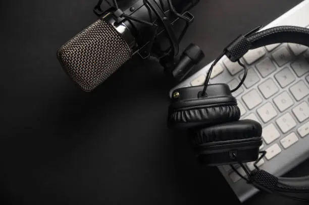 Photo of Flat lay, Studio microphone with professional headphones on a PC keyboard. Black on a black background. Podcasts, radio, streams, blogging, working with sound, recording tracks