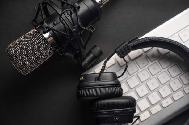 istock Microphone for podcasts and studio headphones on a PC keyboard on a black background, horizontal frame 1203056310