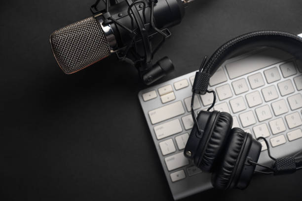 istock Flat lay, Studio microphone with professional headphones on a PC keyboard. Black on a black background. Podcasts, radio, streams, blogging, working with sound, recording tracks 1203056410