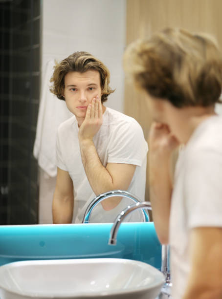 istock young man looking in the mirror,combing his hair,looking at problems on face 1203067465