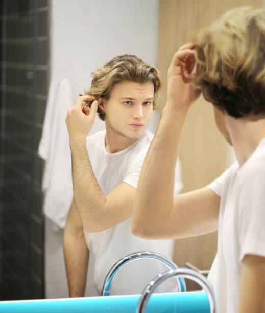 istock young man looking in the mirror,combing his hair,looking at problems on face 1203067474