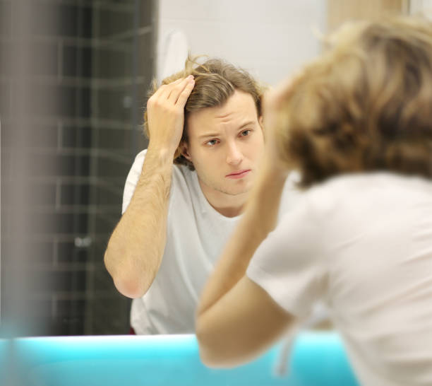 istock young man looking in the mirror,combing his hair,looking at problems on face 1203067479