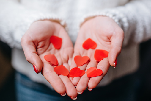 Woman holds many red hearts in her palms, close-up of hands.