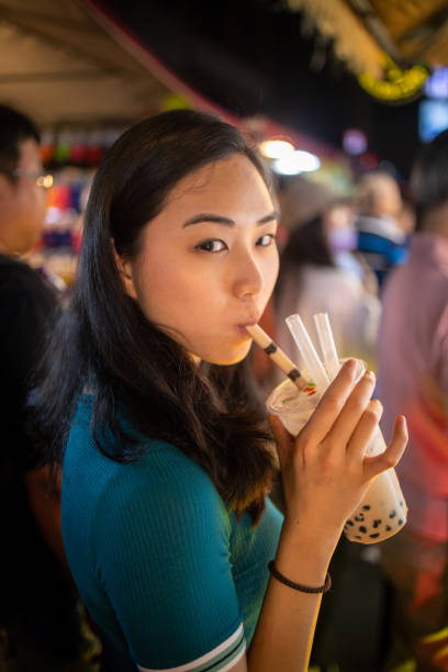 istock Young woman drinking Tapioca ice tea at night market 1203073382