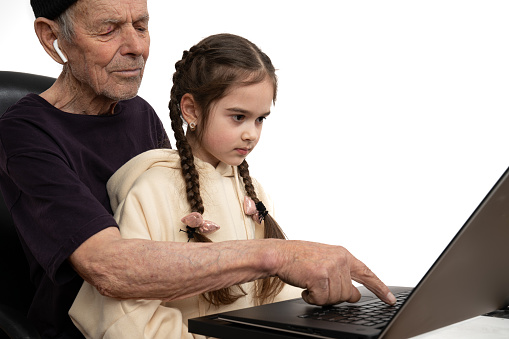 Stylish old man in black hat and t-shirt teaches his granddaughter programming by using laptop, isolated over white background, studio photo