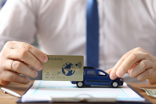 Close-up of bsuinessman hand holding plastic golden credit card. Blue car model on wooden table. Trading and bying transport on internet. Business concept