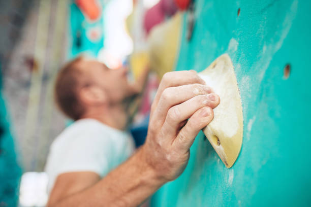 Close-up shot of chalk (magnesium) covered man's palm clinging the indoor climbing grip element while man climbing up. Unfocused climbers face on background. Active sporty people concept image. toma de primer plano de tiza (magnesio) cubierta de la palma del hombre aferrándose al o de agarre de escalada interior mientras el hombre sube. los escaladores desenfocados se enfrentan en el fondo. imagen de concepto de personas deportivas activa