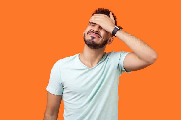 페이스 팜. 손으로 얼굴을 덮는 절망적 인 갈색 머리 남자의 초상화. 오렌지 배경에 고립 된 실내 스튜디오 샷 - crisis 뉴스 사진 이미지