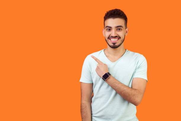 istock Look here! Portrait of positive friendly brunette man pointing at left, empty space for text, advertise. indoor studio shot isolated on orange background 1203078795
