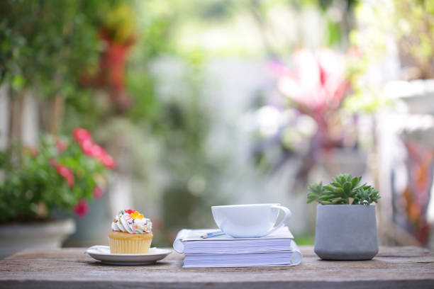 istock White coffee cup with cupcake  and small plant and diary notebook on wooden table at outdoor 1203078961