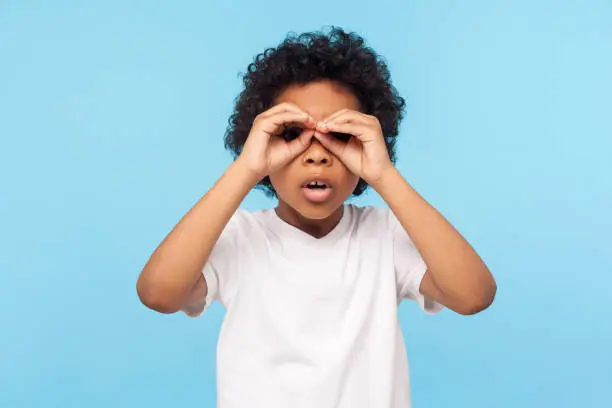 Photo of Curious child exploring world. Portrait of inquisitive nosy little curly boy looking through fingers shaped like binoculars