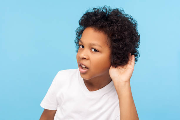 what? i can't hear you. portrait of attentive curious little boy with curly hair holding hand near ear and listening carefully intently - spy secrecy top secret mystery imagens e fotografias de stock