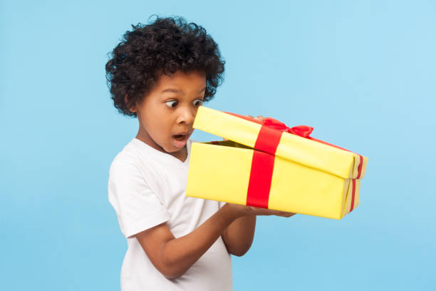 portrait of amazed curious adorable little boy peeking inside gift box, unpacking present with funny astonished expression - christmas child little boys peeking imagens e fotografias de stock