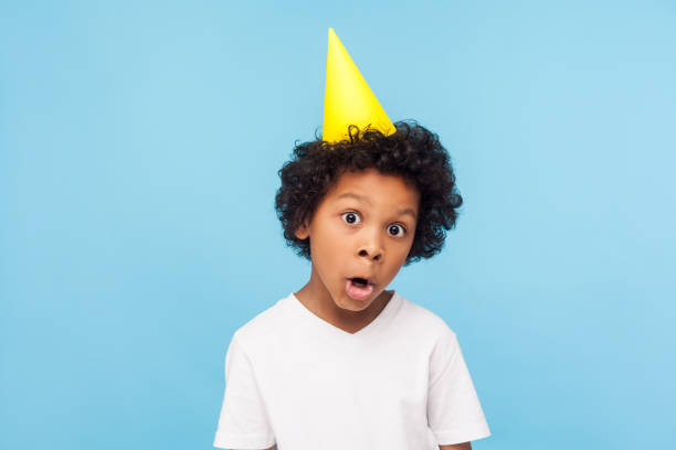 istock Portrait of amusing comical little boy with party cone on head looking at camera with funny amazed grimace 1203079068