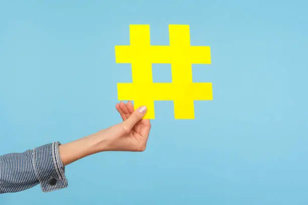 Photo of Closeup of yellow hash sign, female hand holding paper hashtag, symbol of social network trends and popular comments