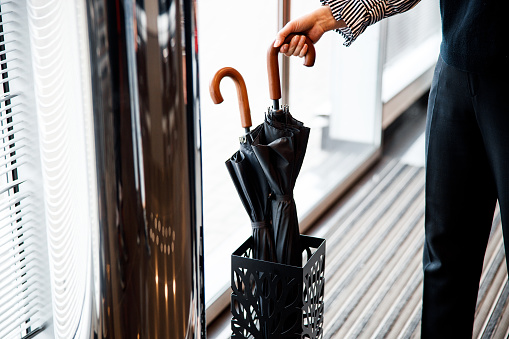 Cropped photo of two black umbrellas in umbrella stand and a woman taking one of them