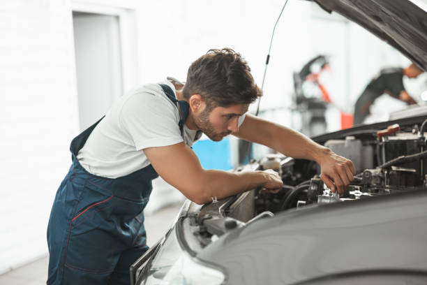 istock young handsome smiling mechanic in uniform fixing motor in car bonnet working in service department 1203083198