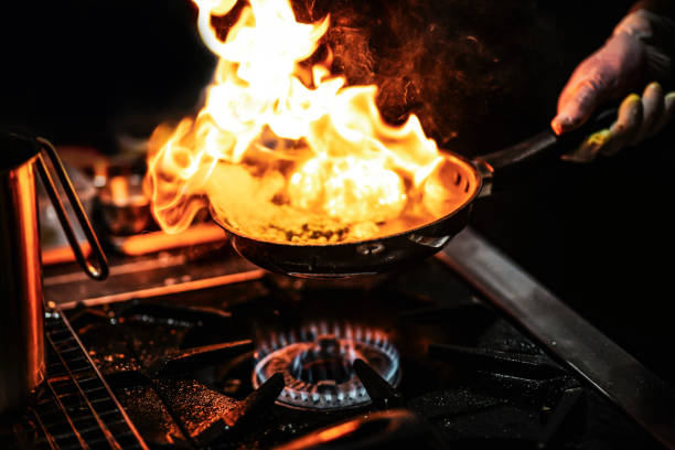 istock Chef cooking with flame in a frying pan on a kitchen stove 1203087418
