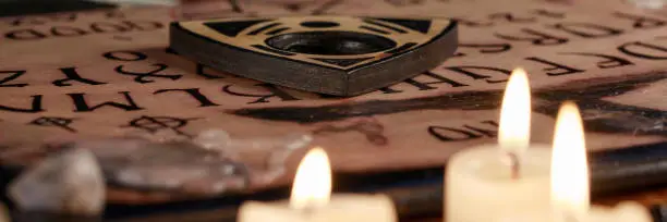 Spiritual board ouija with candles close-up. Mystical ritual of calling dead spirits. Macro. Black magic. Banner.