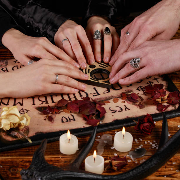 istock People conducting a seance using a Ouija Board, or Talking Spirit Board, with white candles. Shot from overhead. 1203089511