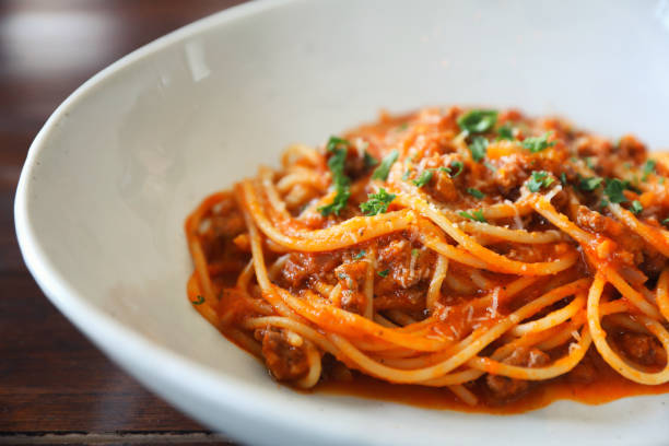spaghetti alla bolognese con carne macinata e salsa di pomodoro guarnita con parmigiano e basilico, cibo italiano - ragù foto e immagini stock