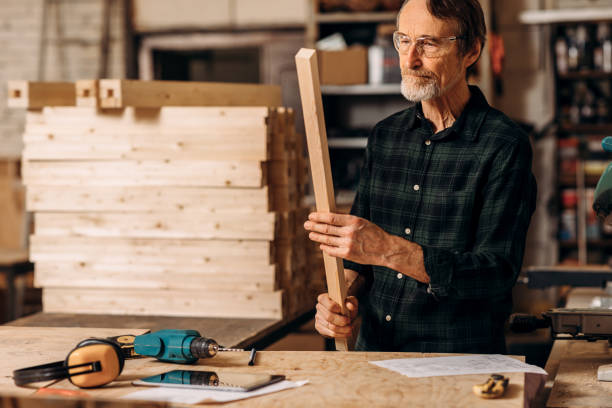 istock Senior carpenter wearing glasses holding a wood plank 1203114914