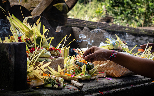 A hand placing burning incense in an offering at a Balinese temple.