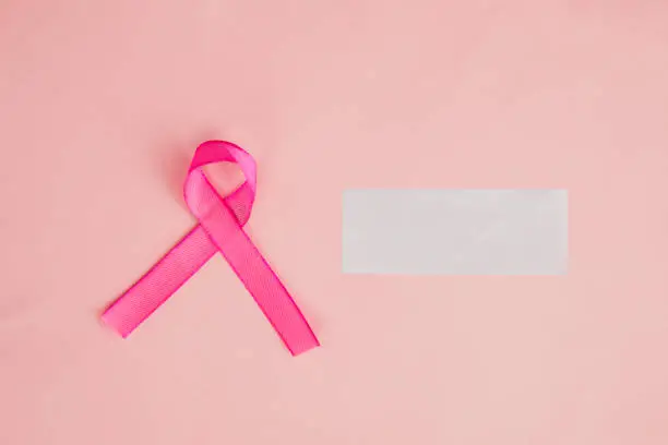 Flat layout of pink ribbon beside a piece of transparent paper, isolated in pink paper background