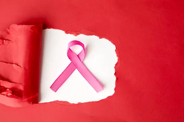 Flat layout of a pink ribbon in a hole of torn red cardboard, isolated in white background