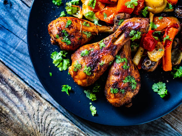istock Roast chicken drumsticks and vegetables served on black plate on wooden table 1203118482