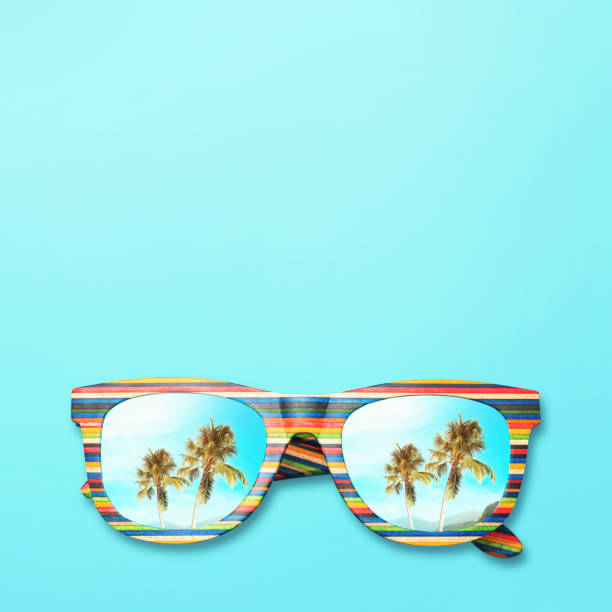 istock Palm trees and mountains are reflected in sunglasses with a multi-colored wooden frame on a blue background, top view. Vacation and travel concept with copy space 1203118613