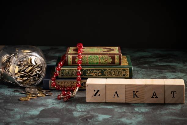 Islamic concept: Zakat ZAKAT wordings on wooden blocks with holy quran and coins in jar sharia stock pictures, royalty-free photos & images