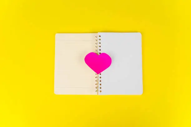 Flat layout of heart shaped card on the middle of the notebook, isolated in yellow background