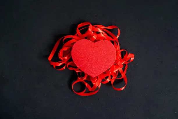 Flat layout of a red valentine box and ribbons, isolated in black wall background