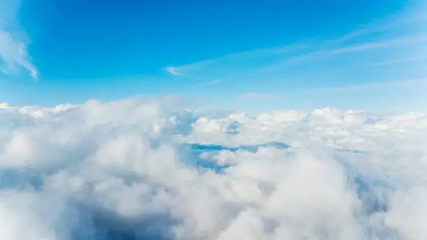 Aerial view of cumulus clouds covering peaks of a mountain with blue sky background