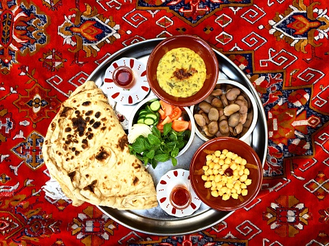 Traditional Arabian Breakfast , Arabian gulf , Kuwait, KSA, Emirates, Oman, Bahrain, Qatar, & Middle East . Includes: “Ash” type of green vegetables, herbs and chickpeas mash , chickpeas, Fava beans, Iranian bread, mint, cucumber, tomato, white onion, and red tea.