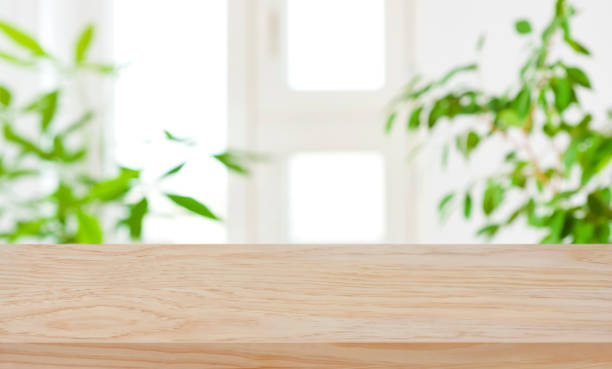 istock Wood table top on blur window and green plants background 1203126759